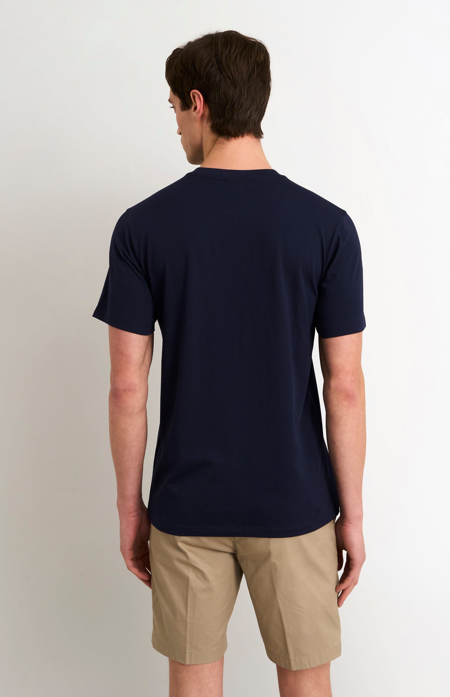 Man wearing a navy blue t-shirt and beige shorts on a plain background