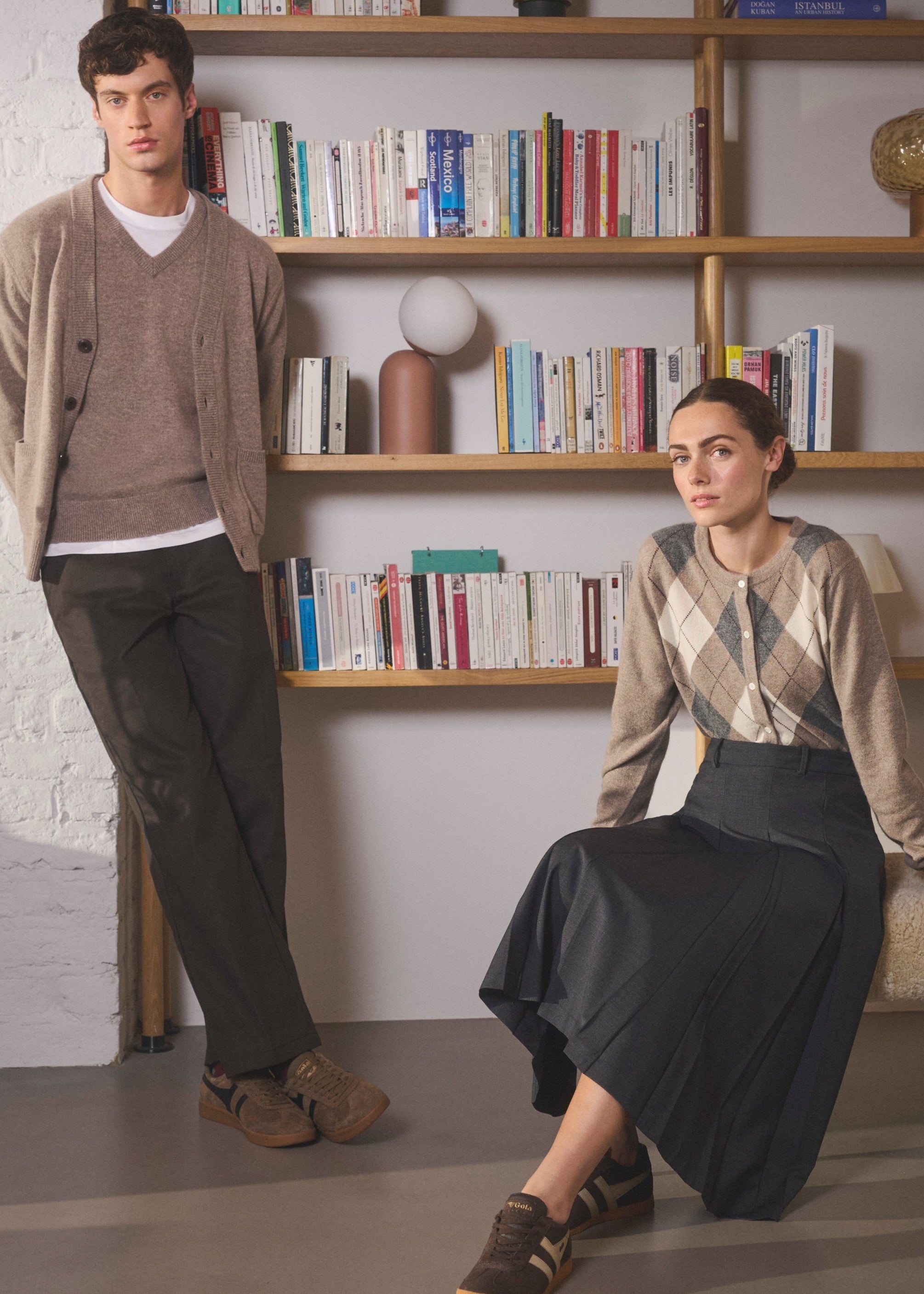 Man and woman wearing Pringle of Scotland cardigans standing in a room with bookshelves and decor.