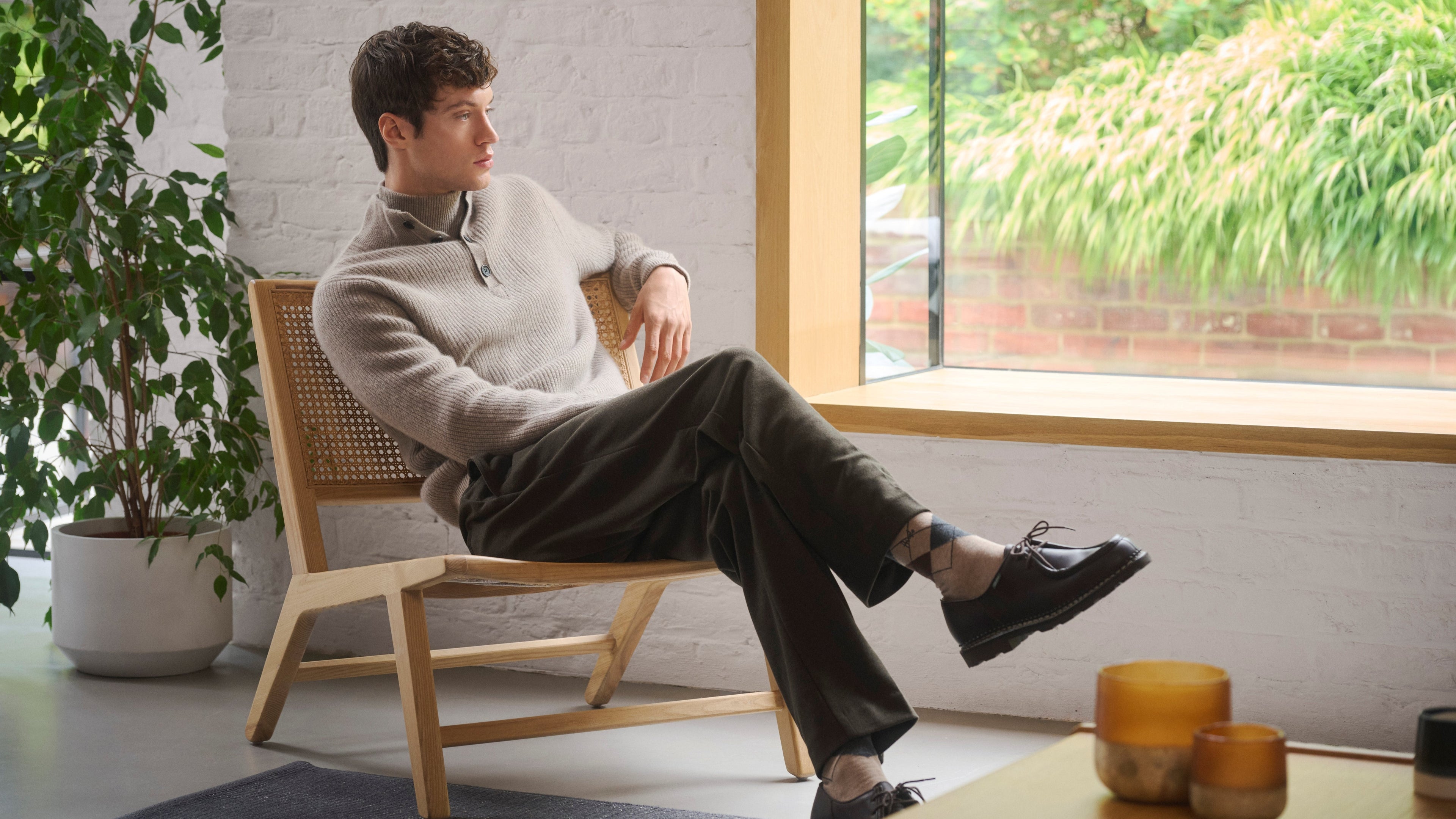 Man sitting on a wooden chair in a room with a large window and plants.