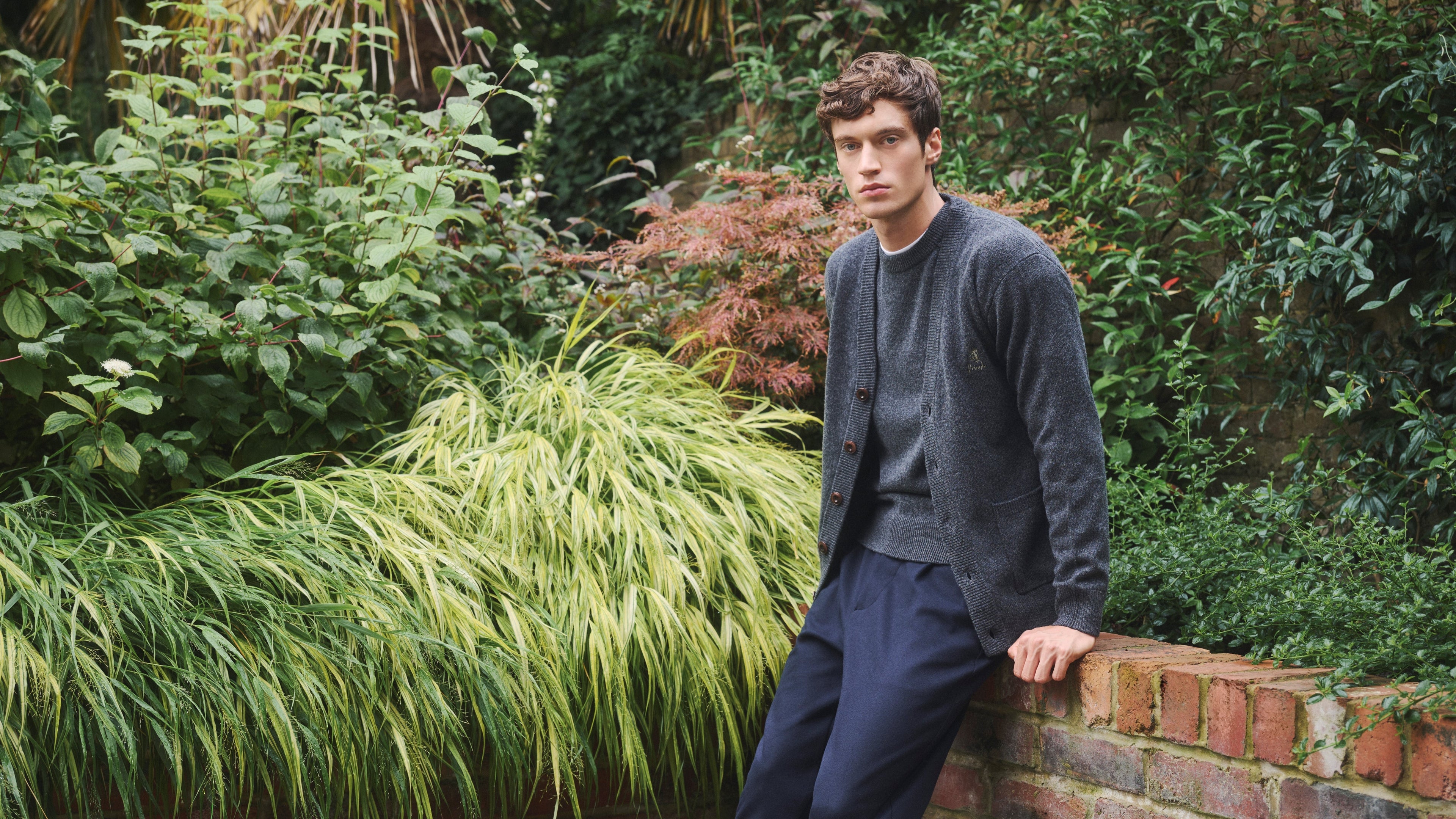 Man leaning against a brick wall in a garden setting wearing Pringle of Scotland supersoft Lambswool Knitwear