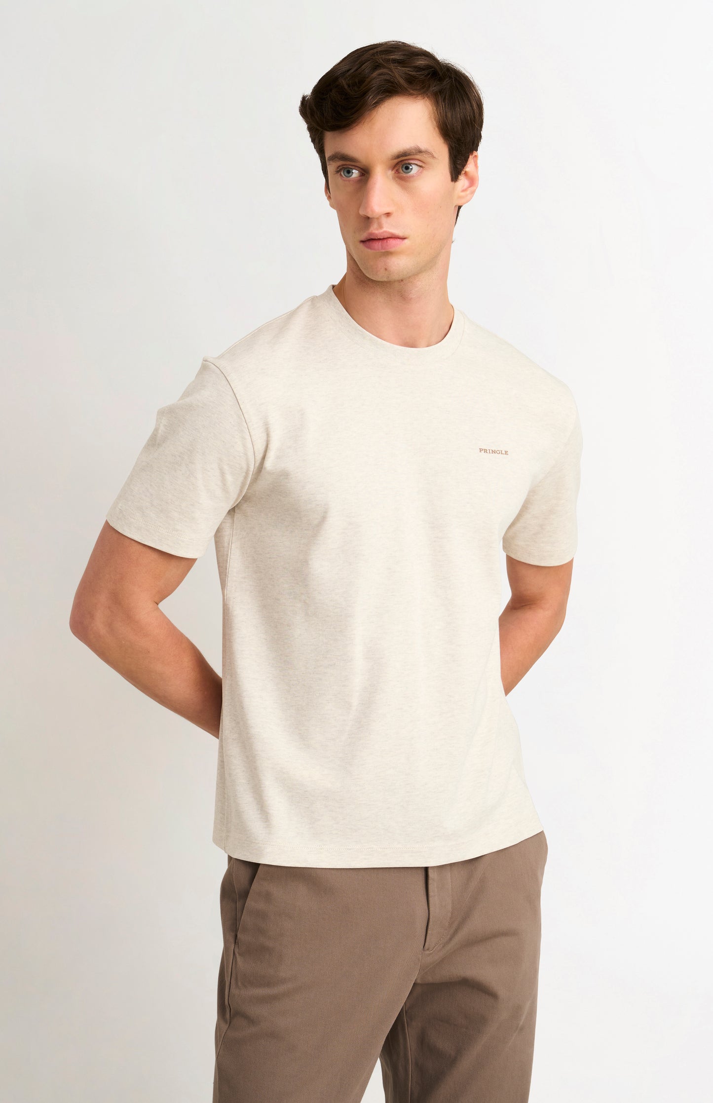 Man wearing a beige t-shirt and brown pants on a white background