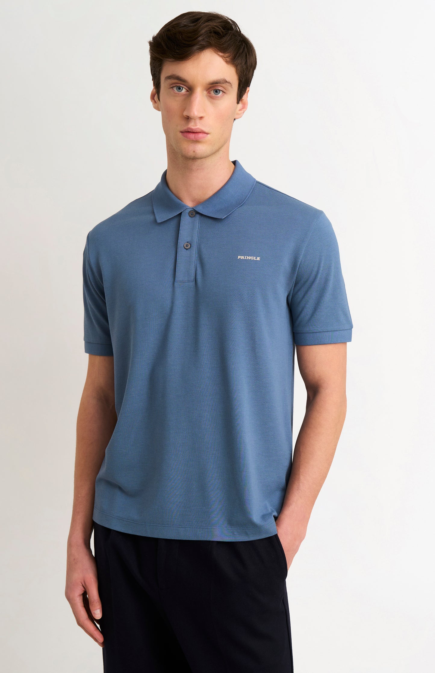 Man wearing a blue polo shirt with dark trousers on a white background