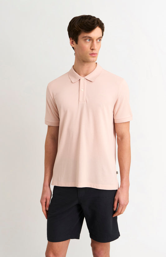 Man wearing a light pink polo shirt and black shorts on a white background