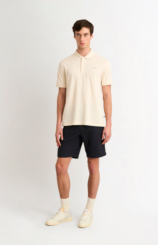 Man wearing an ecru polo shirt with black shorts on a white backrgound