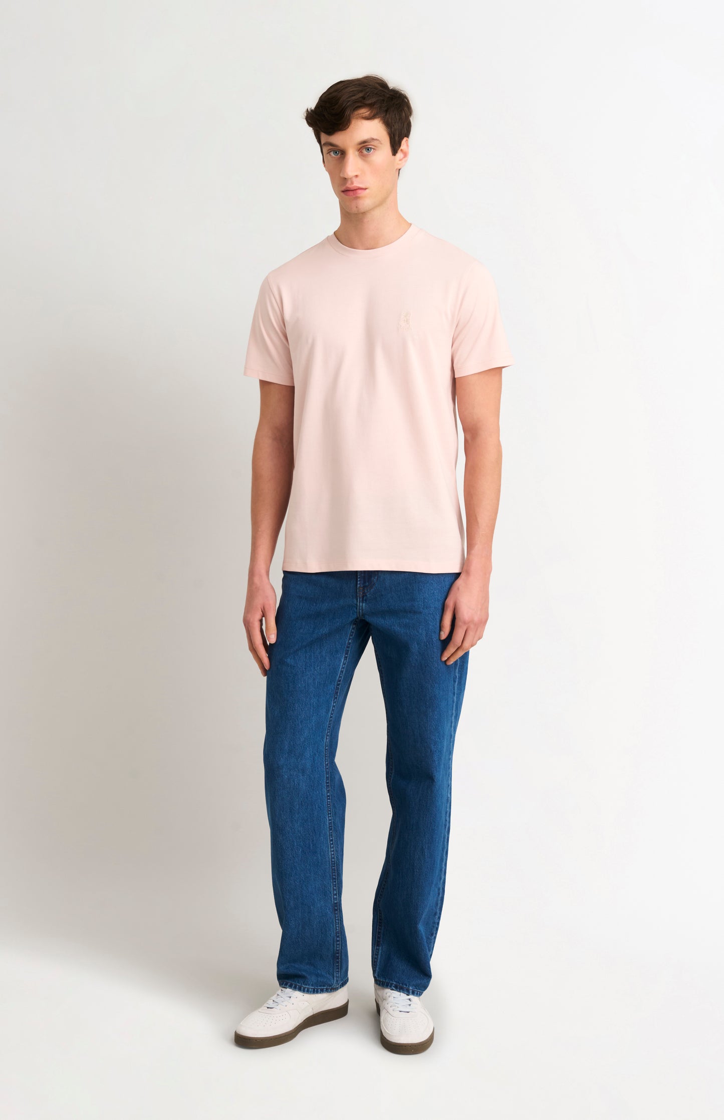 Man wearing a light pink t-shirt and blue jeans on a white background
