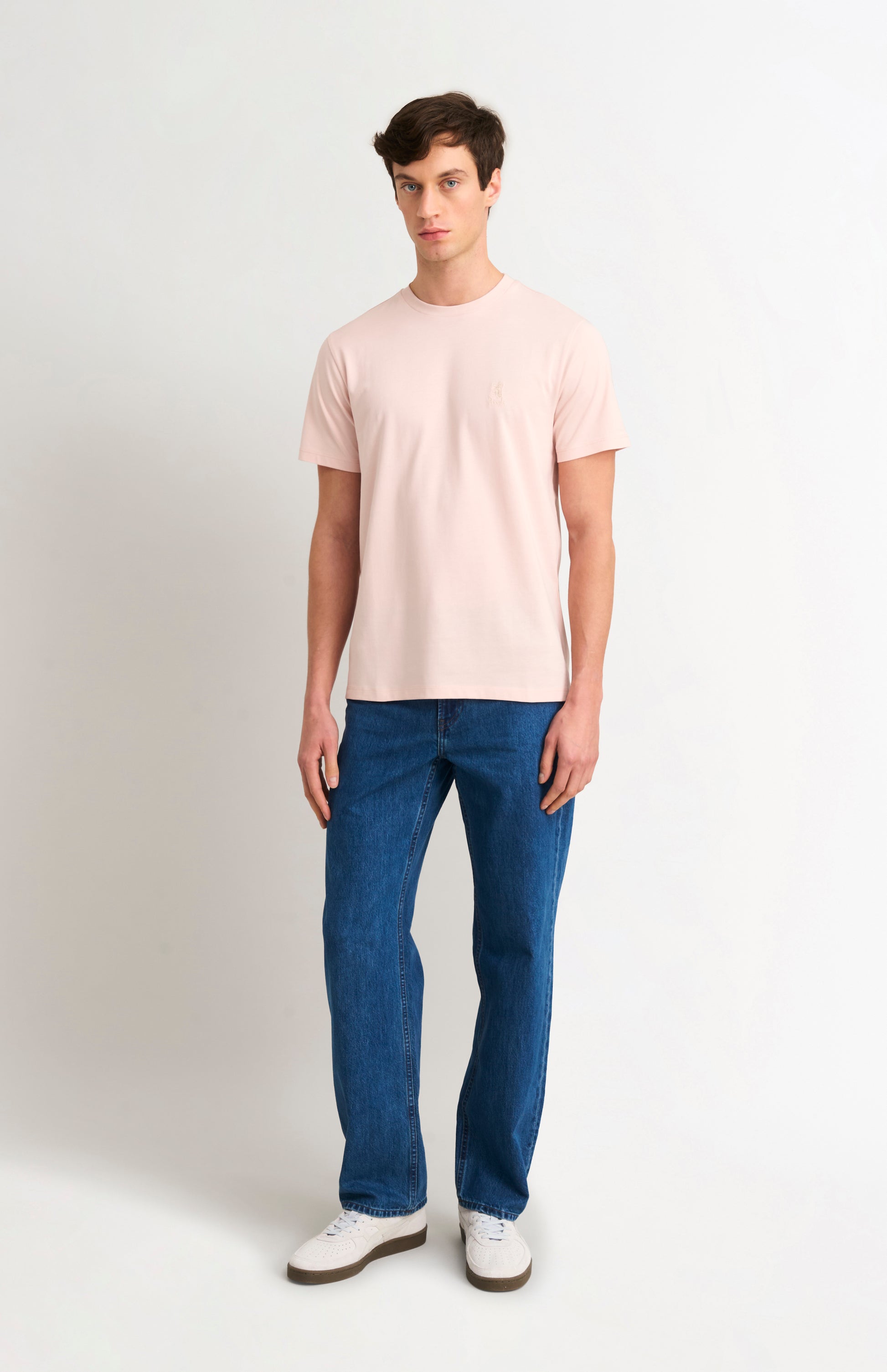 Man wearing a light pink t-shirt and blue jeans on a white background