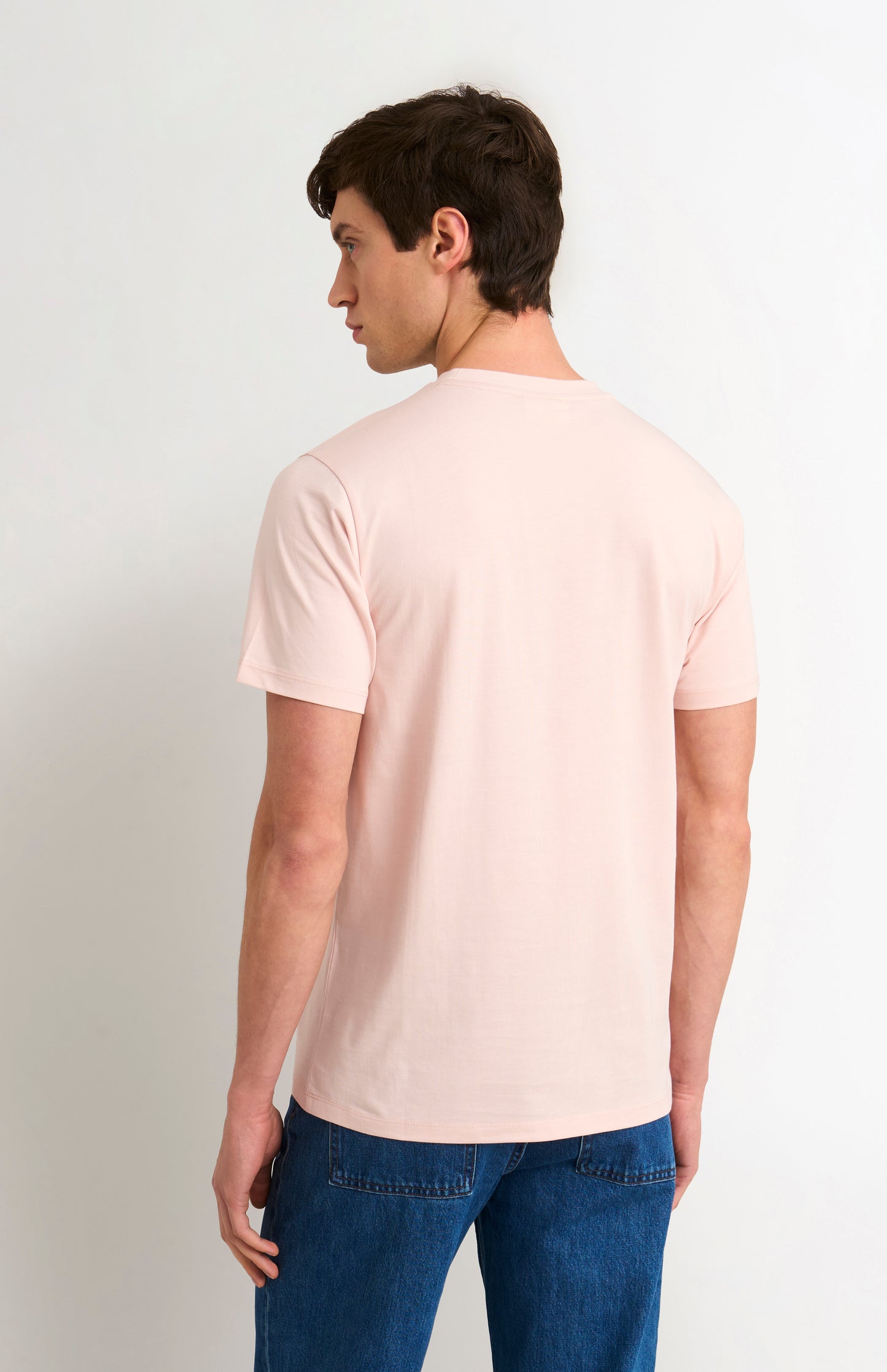 Man wearing a light pink t-shirt and blue jeans on a white background