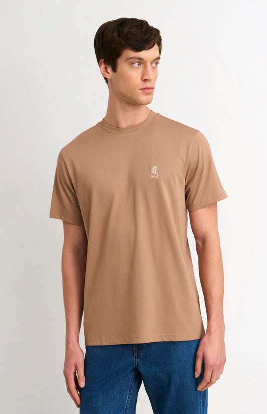 Man wearing a brown t-shirt with a small logo on a plain background