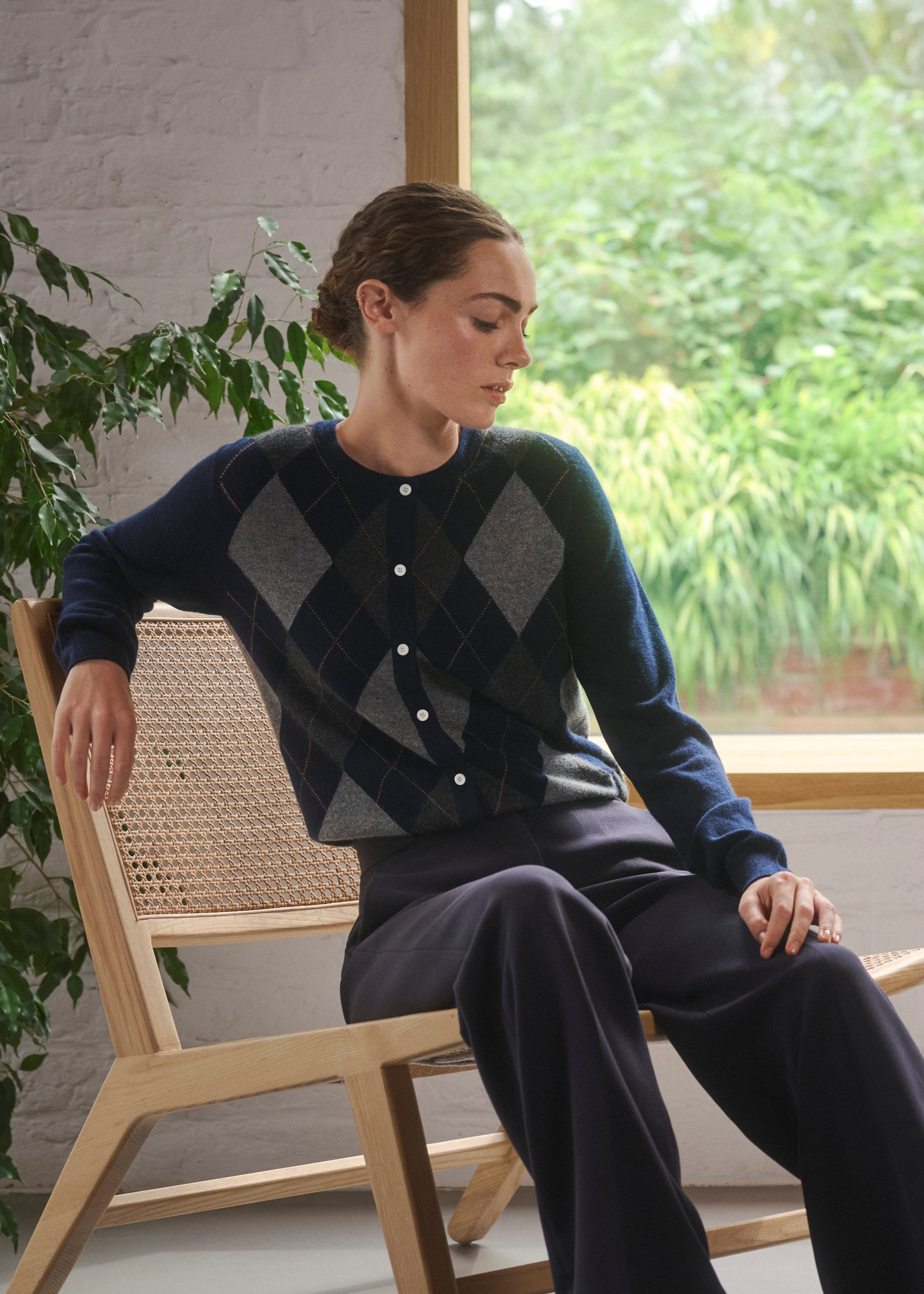 Woman sitting on a chair wearing a blue and grey argyle sweater by Pringle of Scotland
