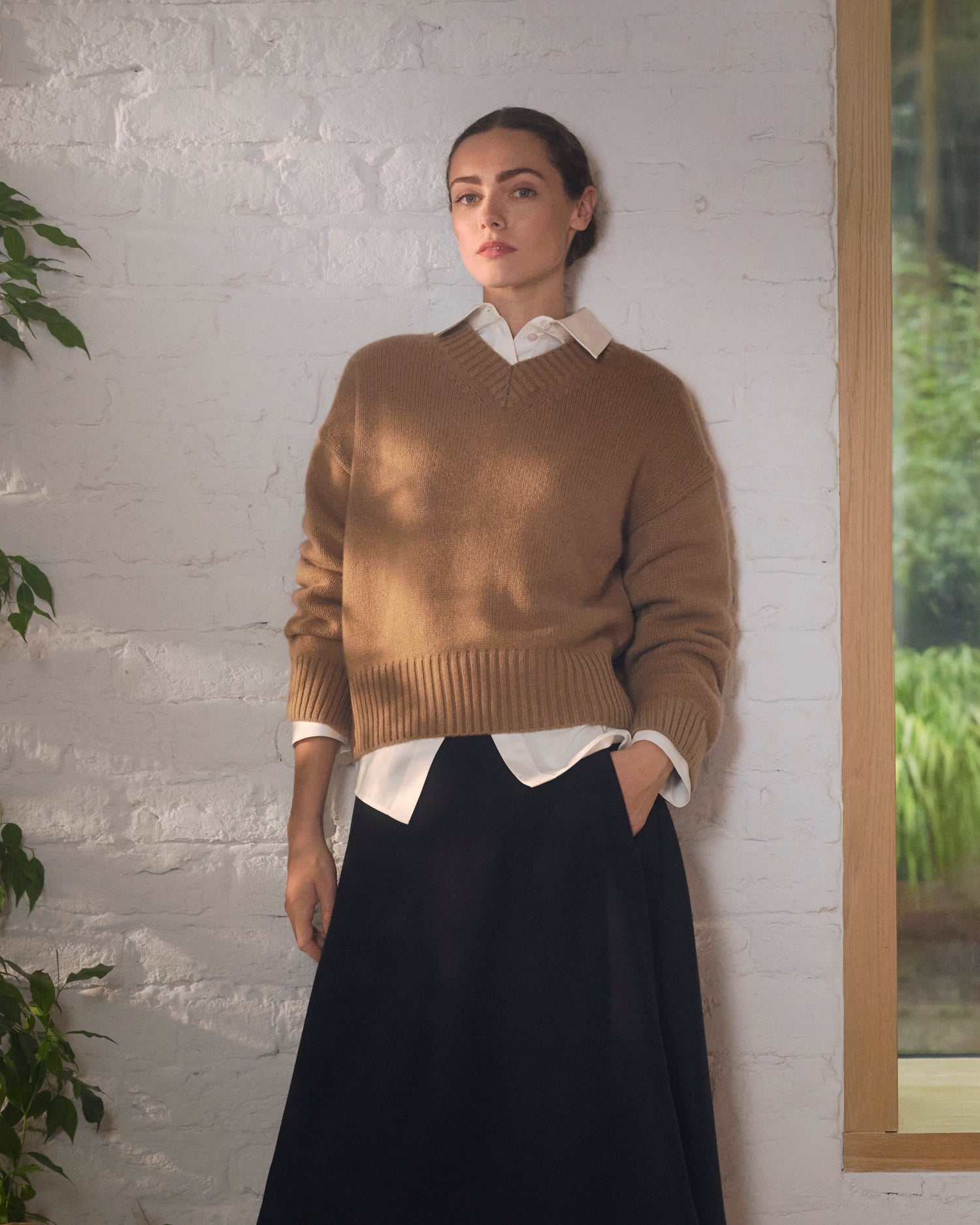 Woman wearing a Pringle camel chunky cashmere jumper next to a window overlooking a garden